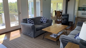 Ein Wohnzimmer mit grauem Sofa, einem Holztisch und einer grauen Couch. Im Hintergrund ist eine Küchenzeile mit Herd und Schränken zu sehen.