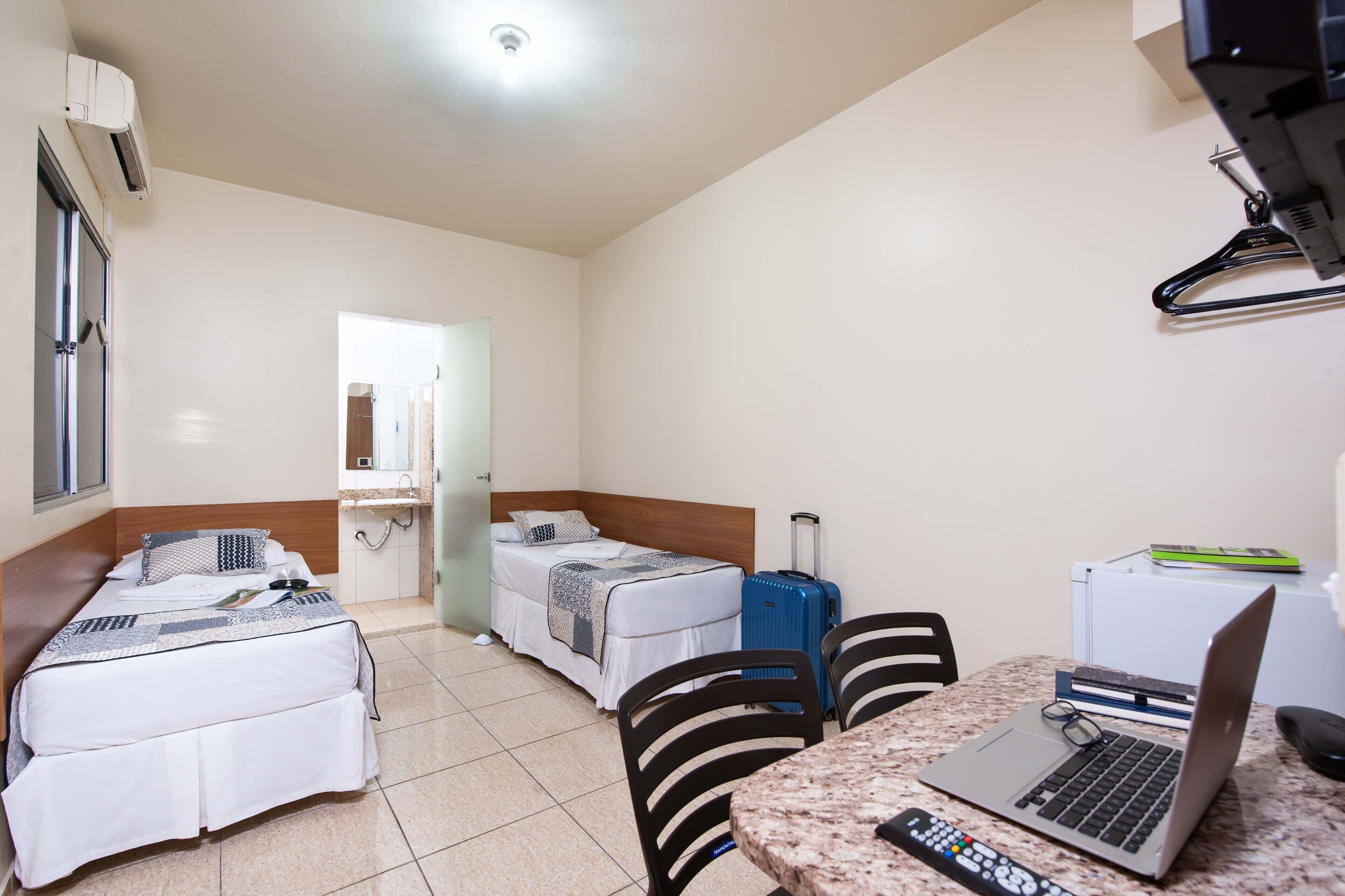Habitación de hotel con dos camas, un escritorio, una computadora portátil, una maleta y un control remoto.