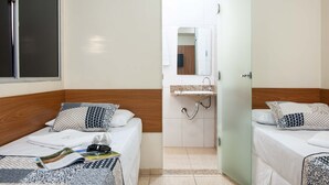 Habitación de hotel con dos camas, un baño pequeño con lavamanos y espejo, y una ventana.