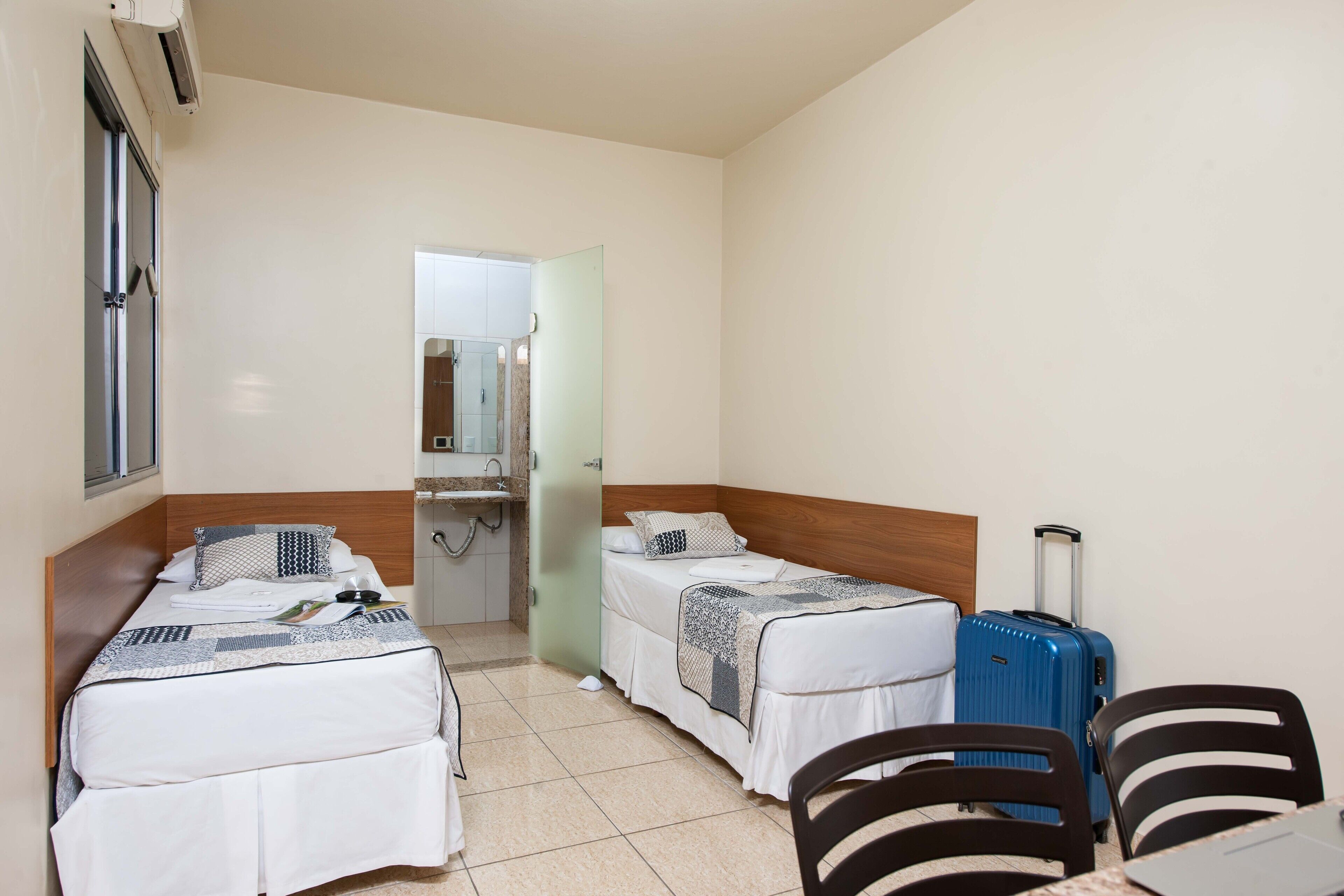Una habitación de hotel con dos camas individuales, un baño con espejo y una mesa con sillas.