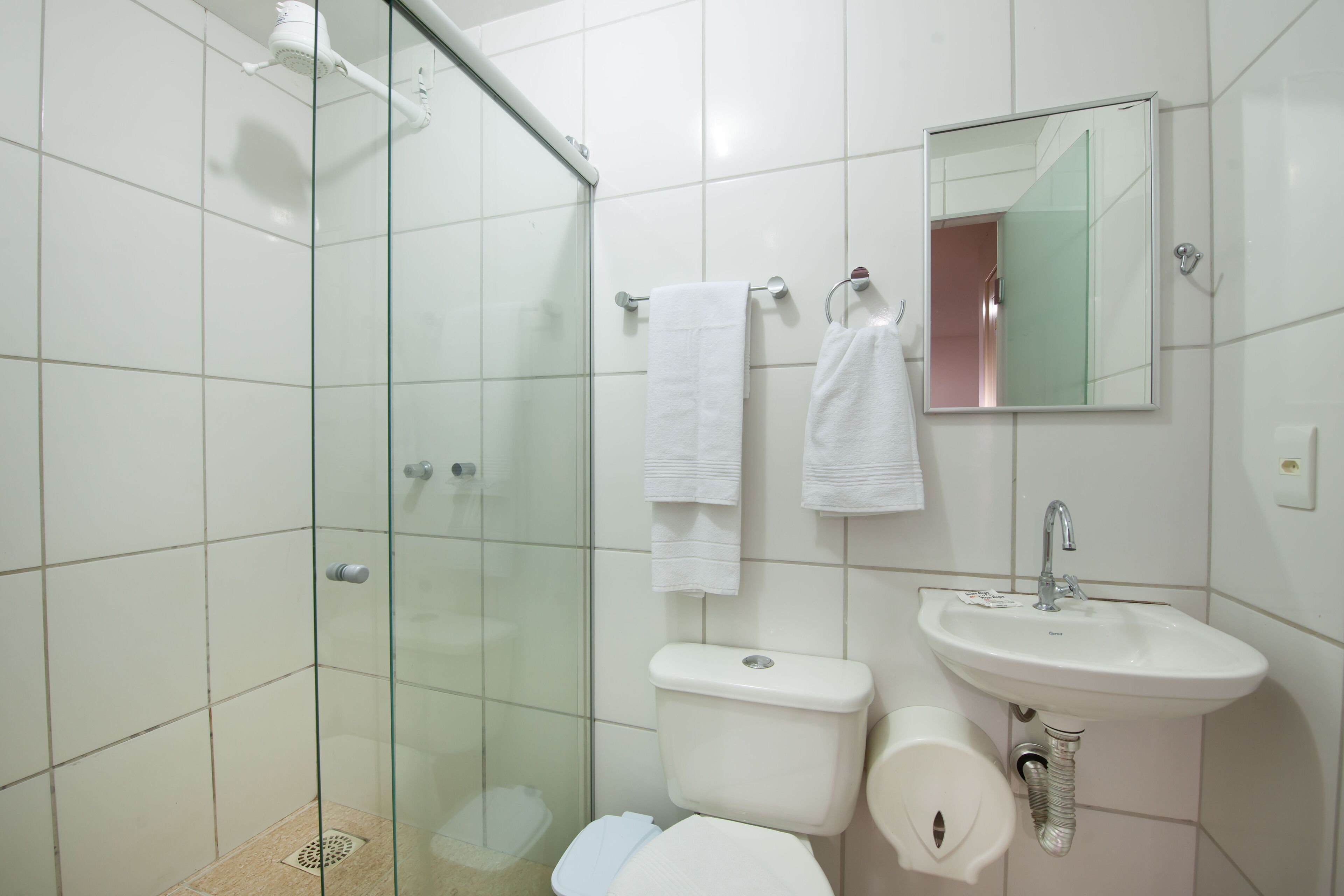 A bathroom with a glass shower enclosure, a toilet, and a sink with a mirror above it.