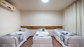 Quarto de hotel com duas camas de solteiro, cabeceira de madeira, ar condicionado e janela com cortinas.