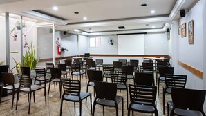 Un salón de conferencias con filas de sillas, una pizarra y una pantalla de proyector.