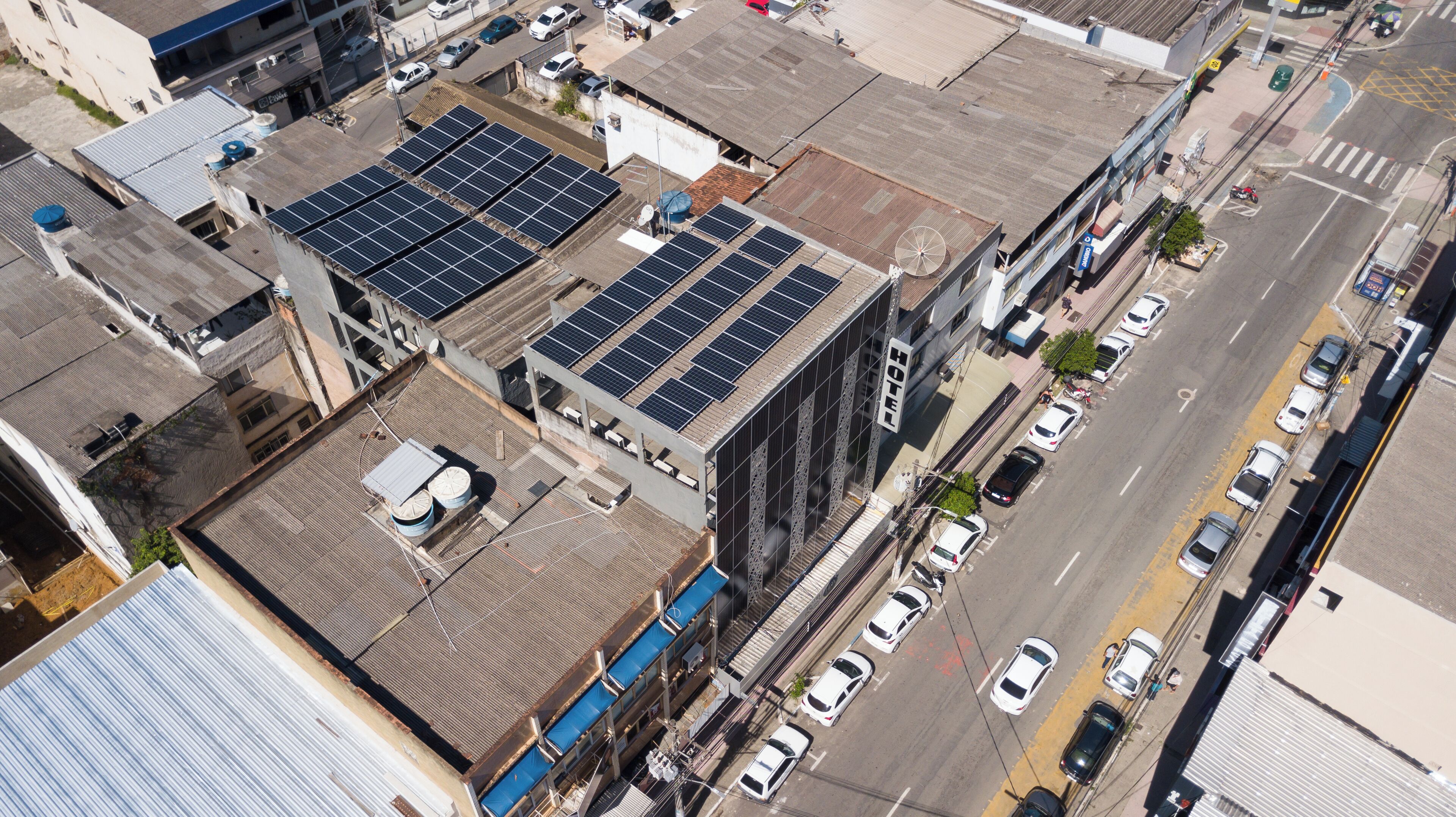 A hotel with multiple floors, solar panels on the roof, and a street with cars.