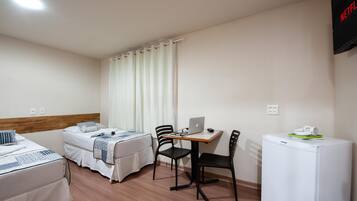 Habitació d'hotel amb dos llits, una escriptori amb un ordinador portàtil, cadires i un frigorífic.