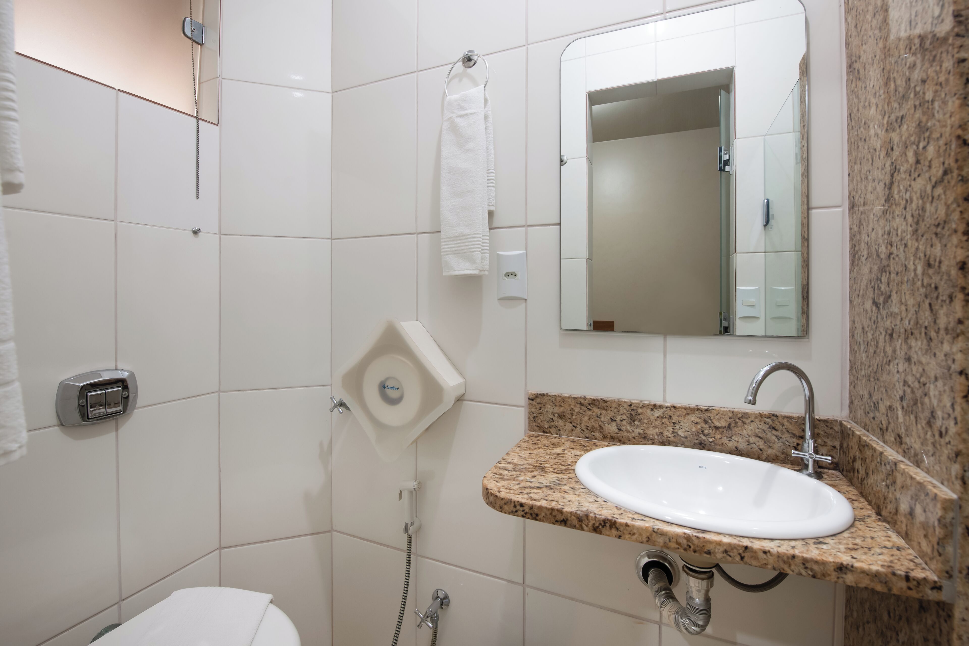 Un baño con inodoro blanco, lavamanos con encimera de granito, espejo y barra para toallas.