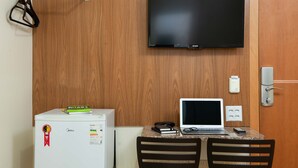 Habitación de hotel con una televisión de pantalla plana montada en la pared, un escritorio pequeño con una computadora portátil, un refrigerador y un enchufe.