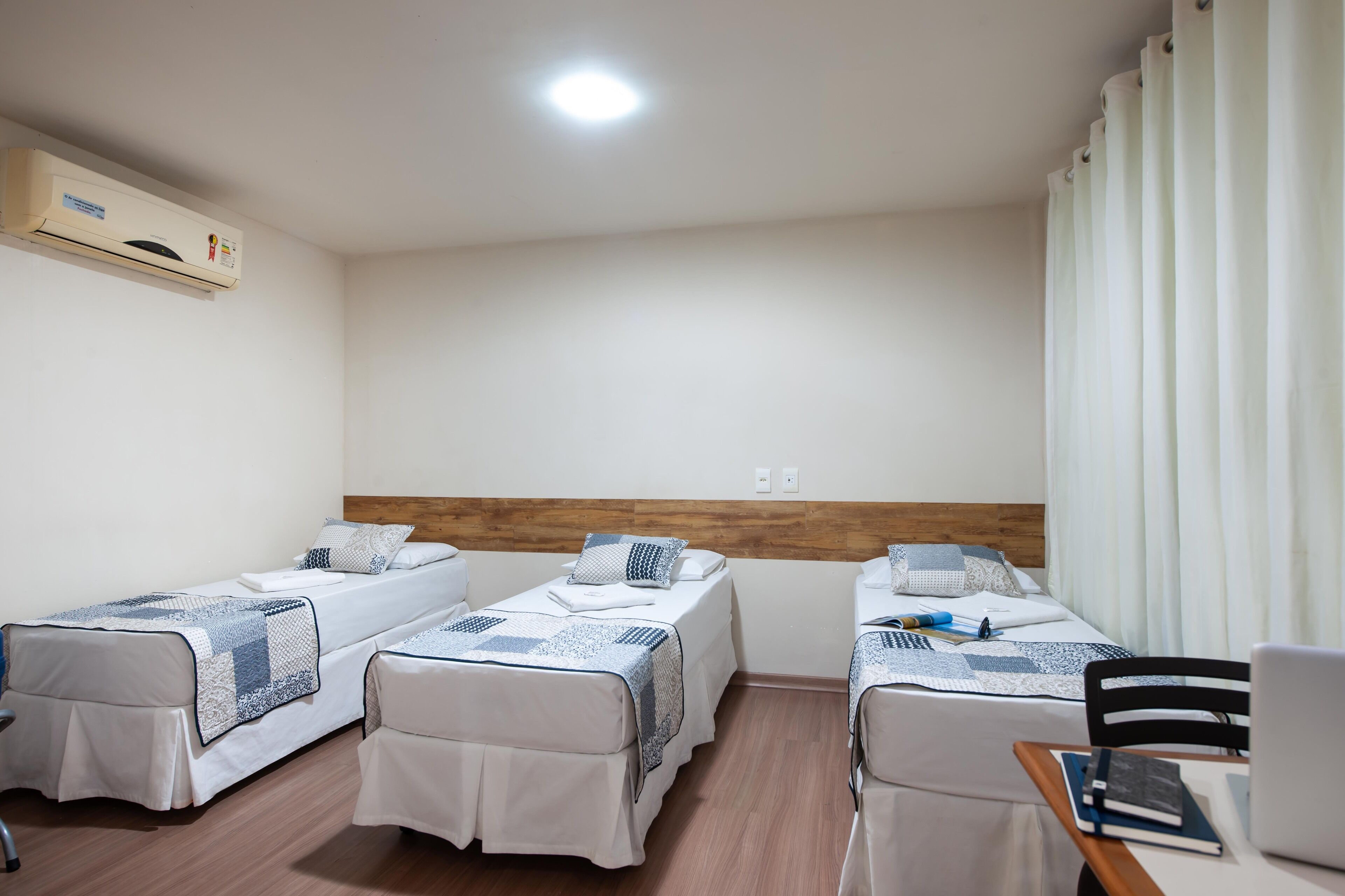 Une chambre d’hôtel avec trois lits simples, un bureau avec une chaise, un ordinateur portable et un carnet.