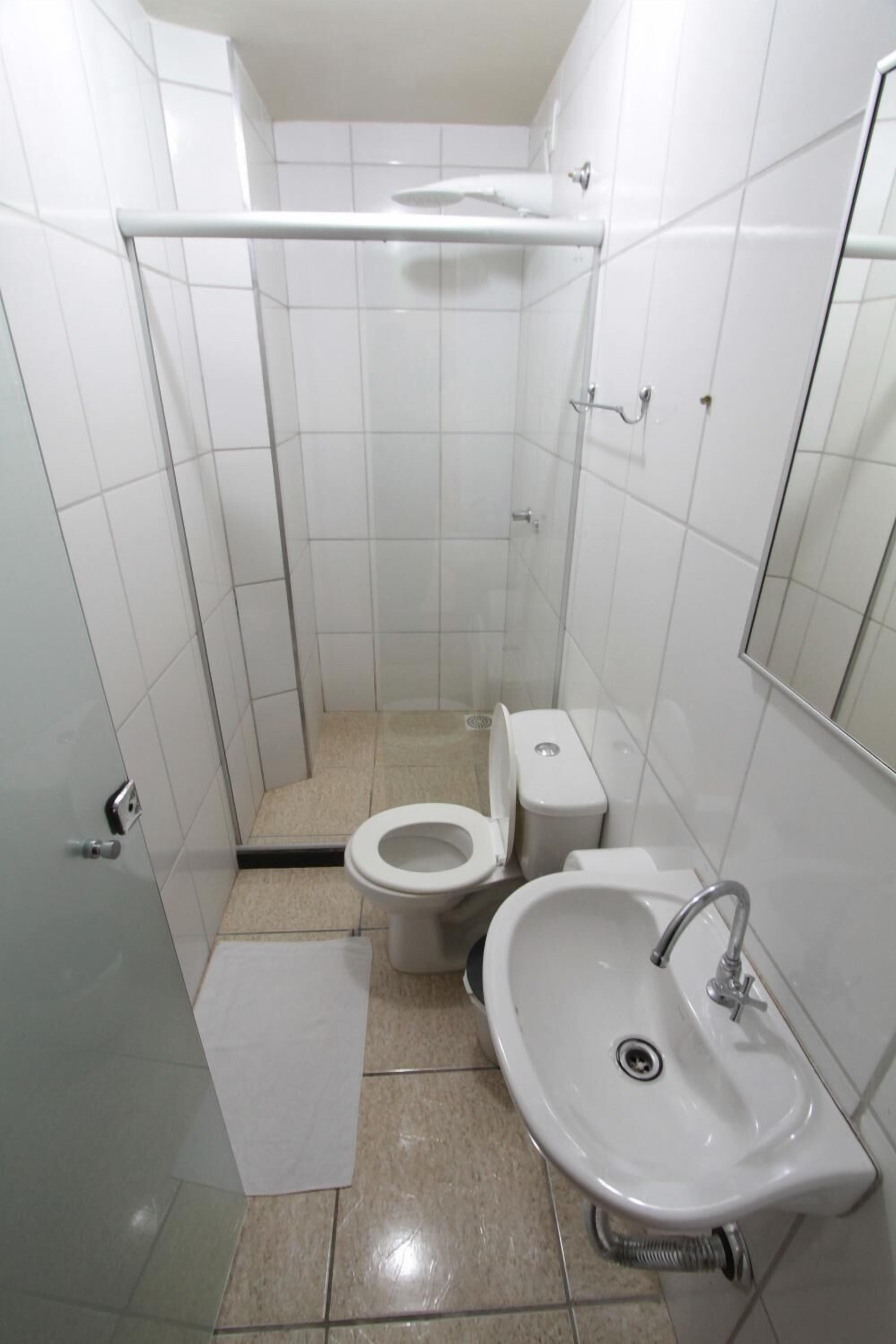 A small, clean bathroom with white tiles, a toilet, a sink, and a shower area.