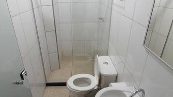 A small, clean bathroom with white tiles, a toilet, a sink, and a shower area.