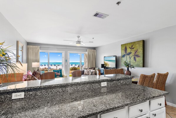 A modern kitchen with granite countertops, a ceiling fan, and a view of the beach.