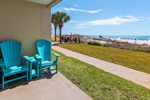 A patio with turquoise Adirondack chairs, a paved walkway, and a view of the beach with umbrellas.