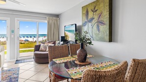 A dining area with a glass table, wicker chairs, a vase, and a painting. - Beach Service Included! | 1BR Windancer 111 | Beachfront | Heated Pool | 1st Flo (Miramar Beach)