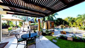A covered outdoor area with a pool, patio furniture, and a thatched-roof structure.