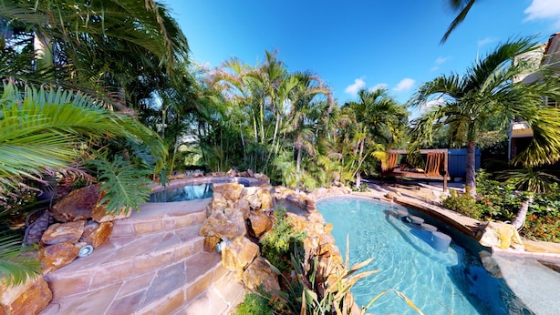 A pool surrounded by tropical vegetation and rocks, with a wooden deck and a hammock.