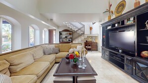 A spacious living room with a large sectional sofa, a flat-screen TV, and a staircase leading to an upper level.