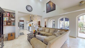 A spacious living area with a sofa, coffee table, and bookshelf. A kitchen is visible in the background with a washing machine.