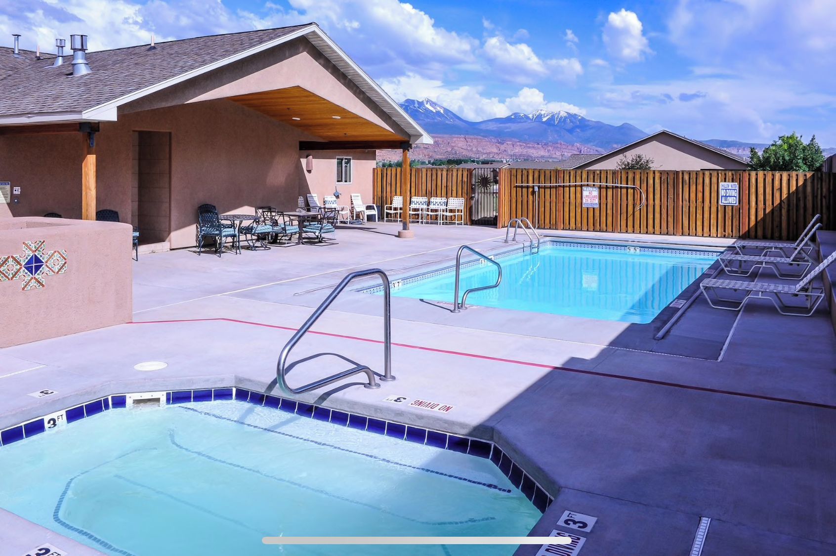 A pool area with a hot tub, lounge chairs, and a view of mountains.