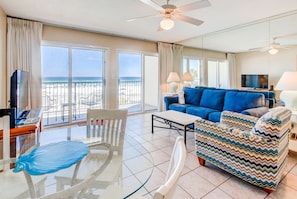 Relax in this stylish living area with a large window offering a view of the beach, a sofa, armchair, and dining table.