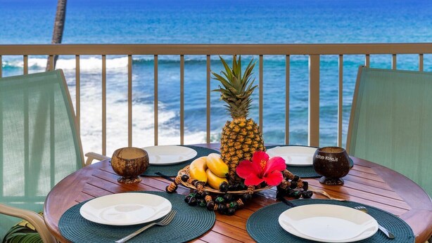 Une table dressée pour deux personnes, avec vue sur l’océan, agrémentée d’un ananas, de bananes et d’une fleur d’hibiscus.