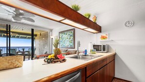 Une cuisine avec un plan de travail en bois, un évier, un four à micro-ondes et une horloge au mur.