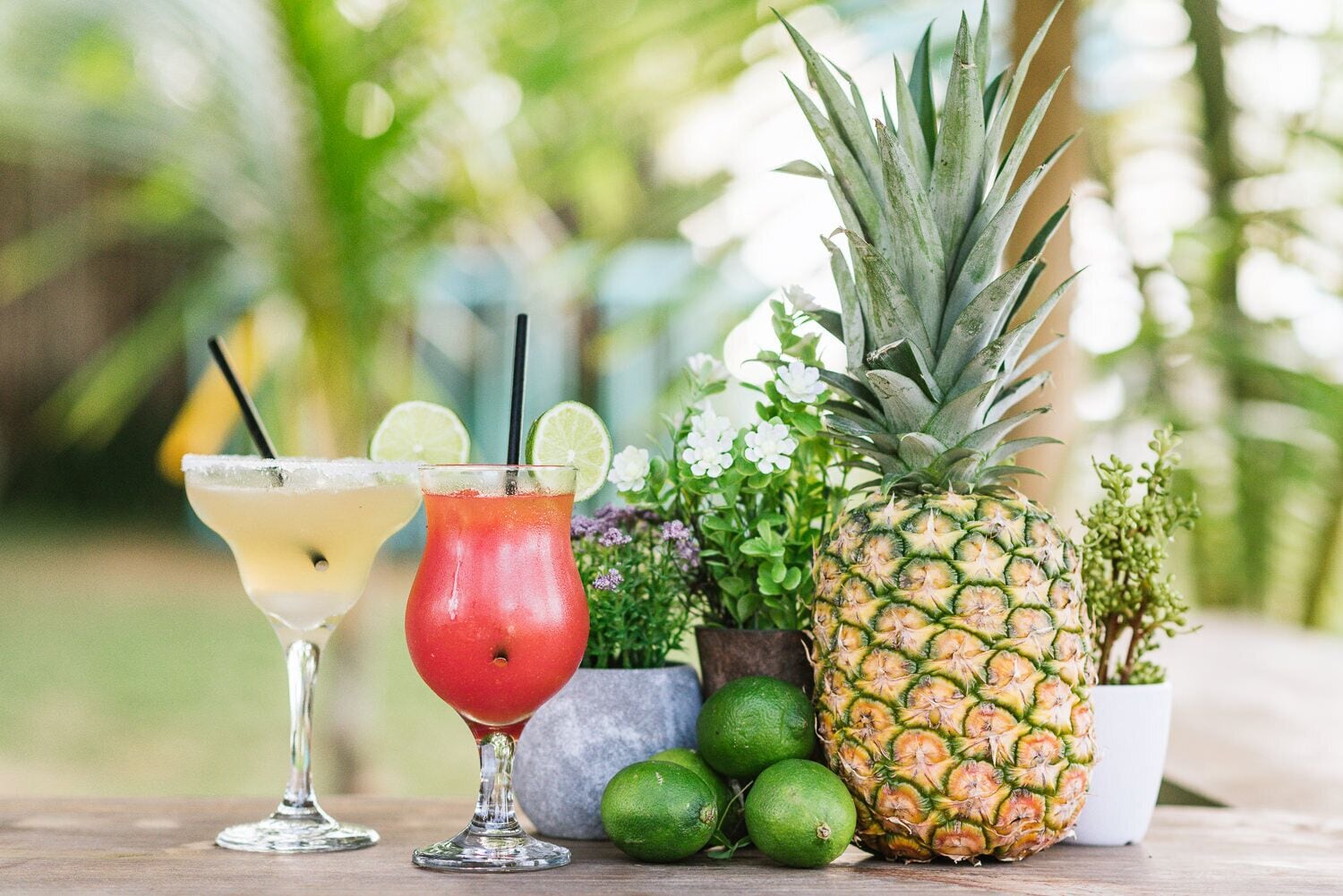 Zwei Cocktails auf einem Holztisch, mit einer Ananas und Limetten in der Nähe.