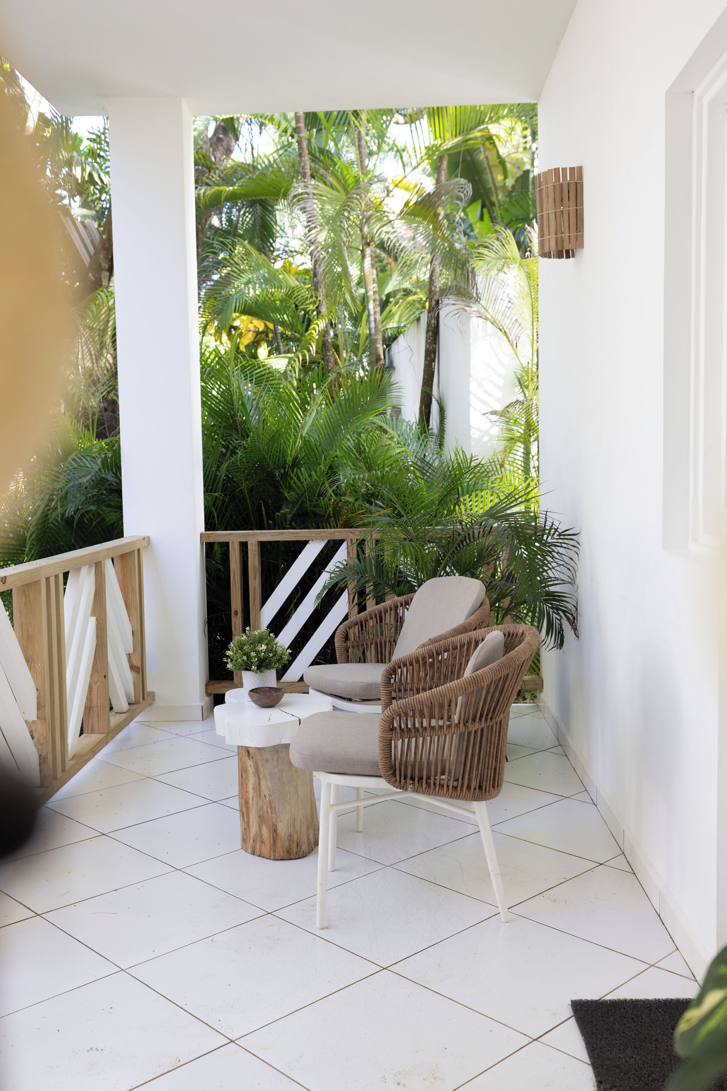 A balcony with a wicker chair, a small table with a plant, and a wooden railing.