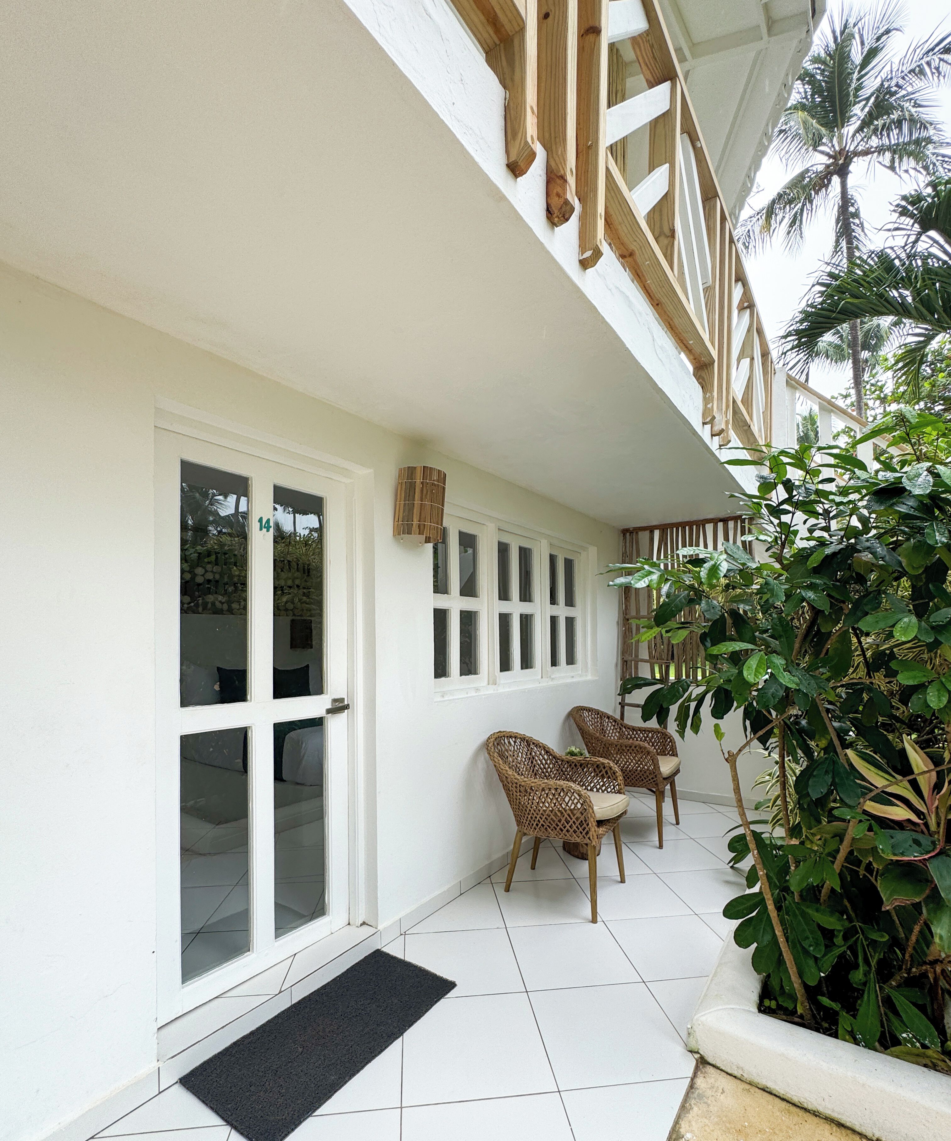 A building with white exterior walls, multiple windows, a balcony with wooden railings, and a black doormat.