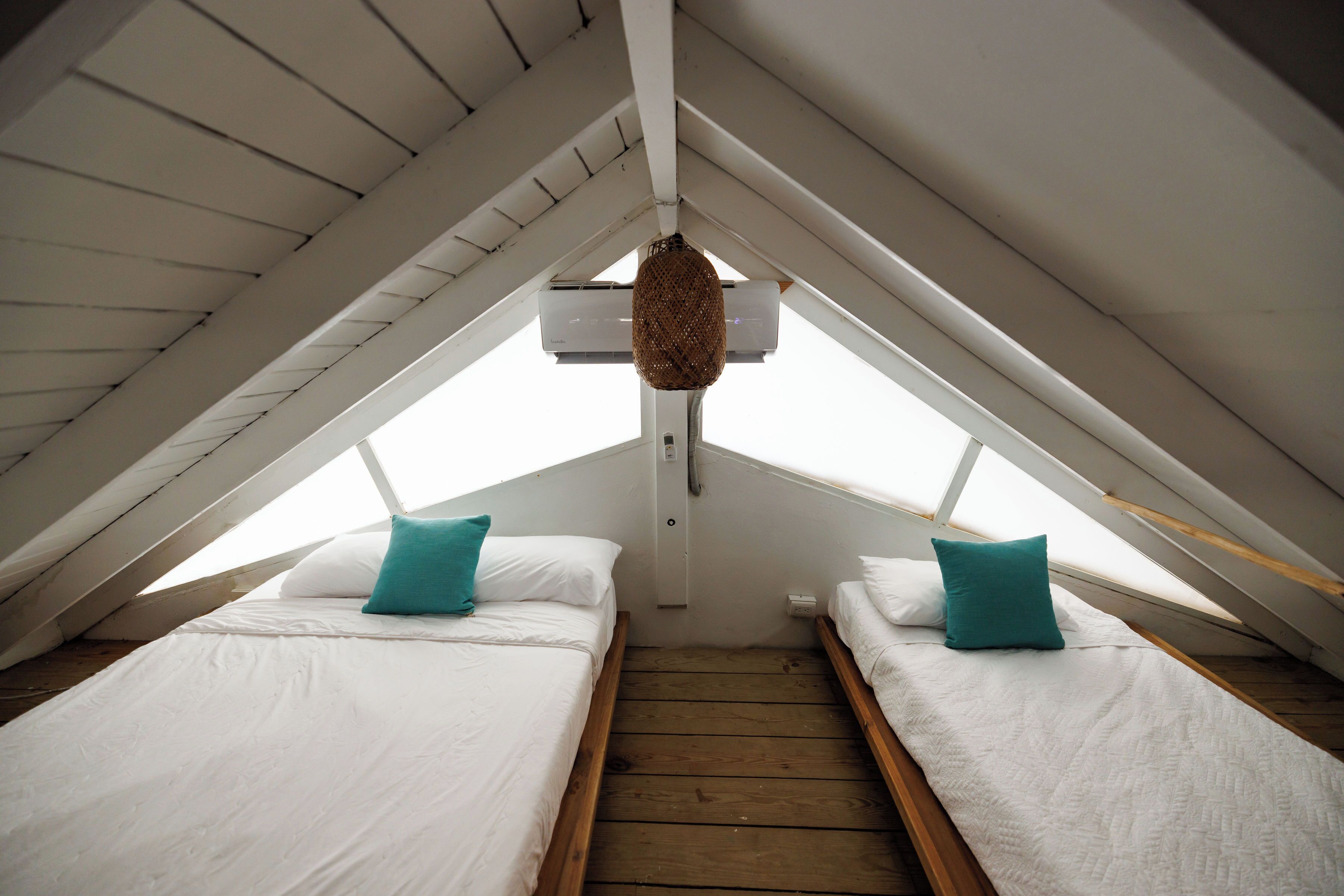 A small attic bedroom with two beds, wooden flooring, and a sloped ceiling.