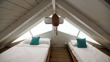 A small attic bedroom with two beds, wooden flooring, and a sloped ceiling.