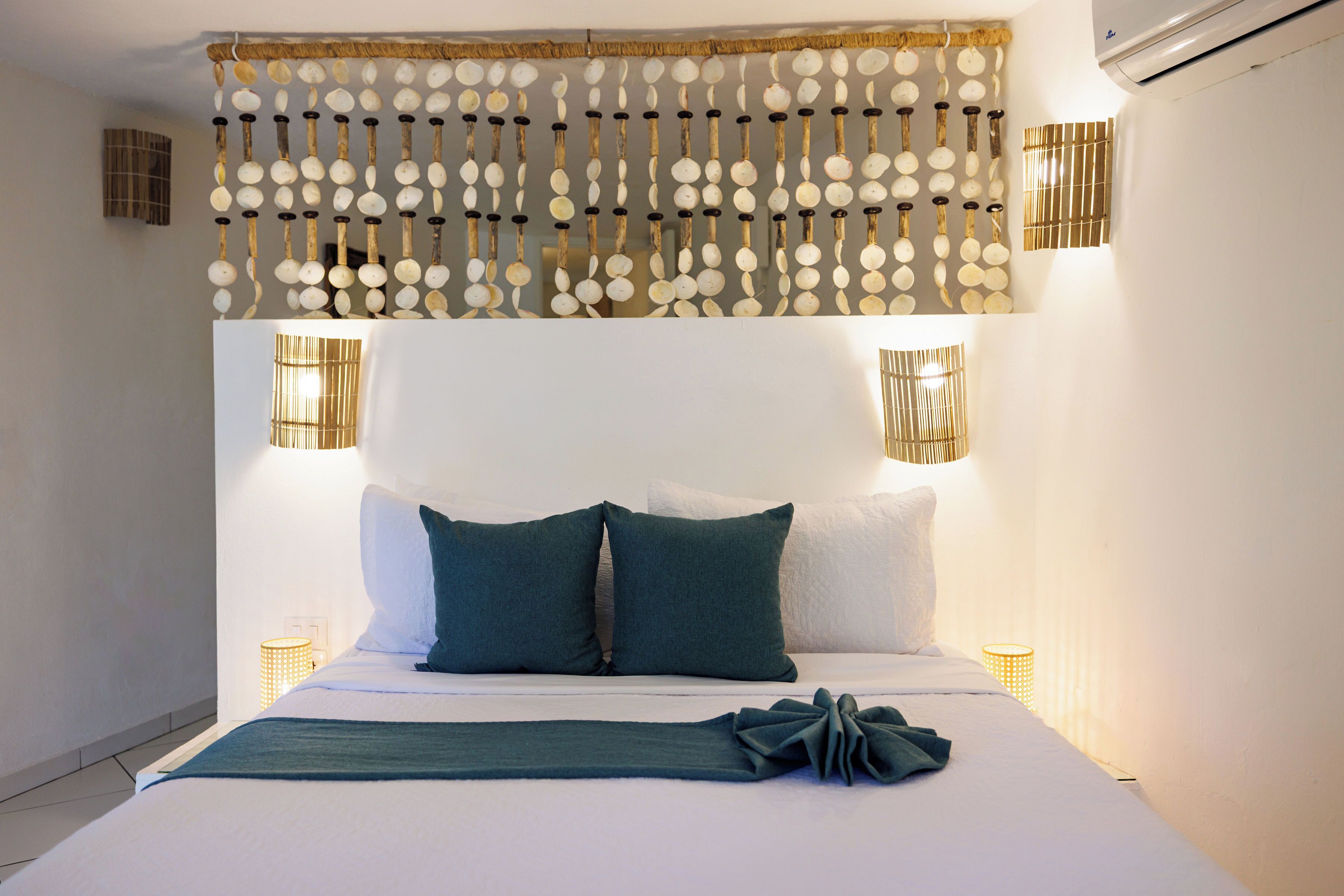A neatly made bed with pillows, a decorative headboard, and wall-mounted lights.