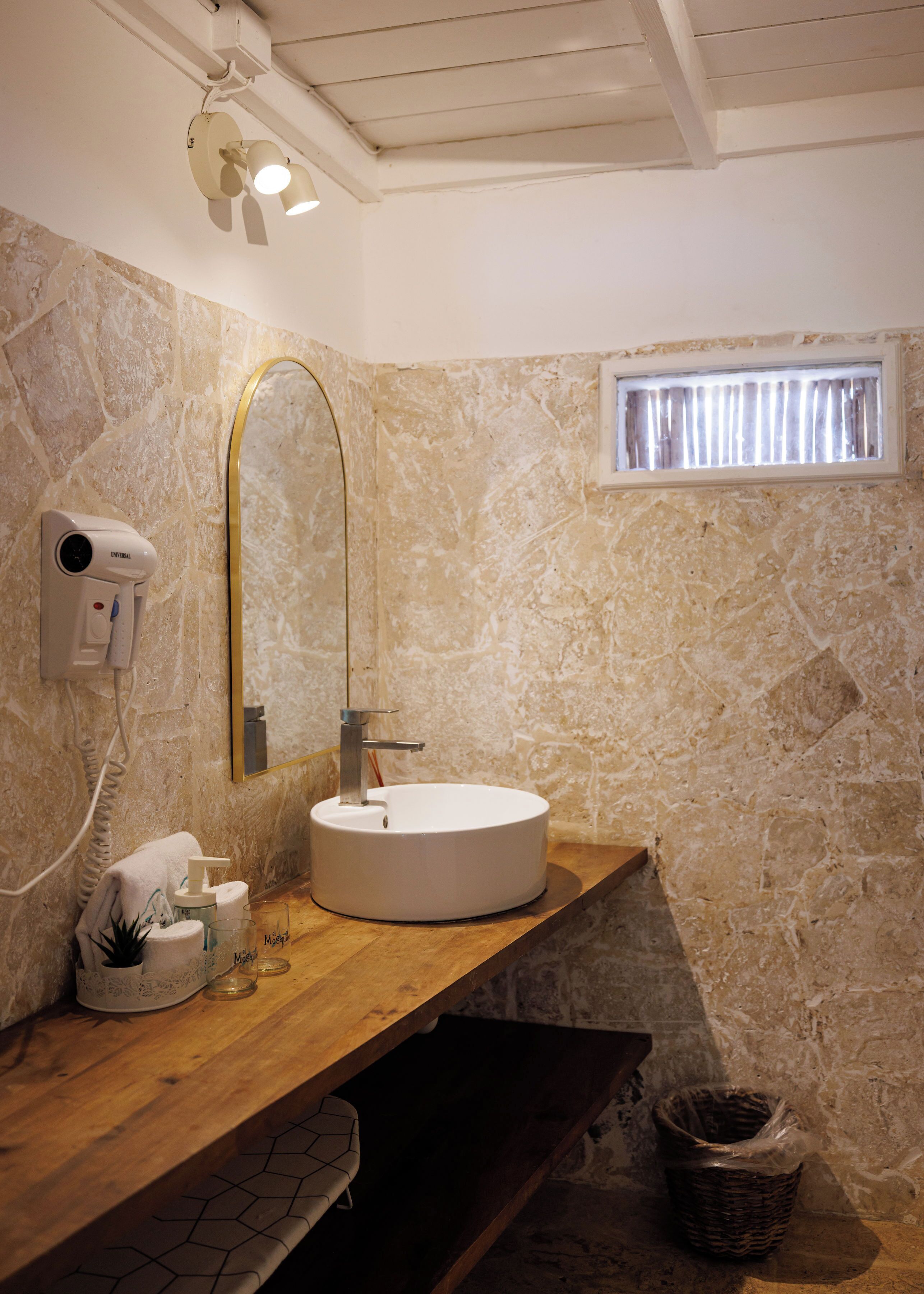 A bathroom with a round sink, a mirror, a towel rack, a hairdryer, and a window with curtains.