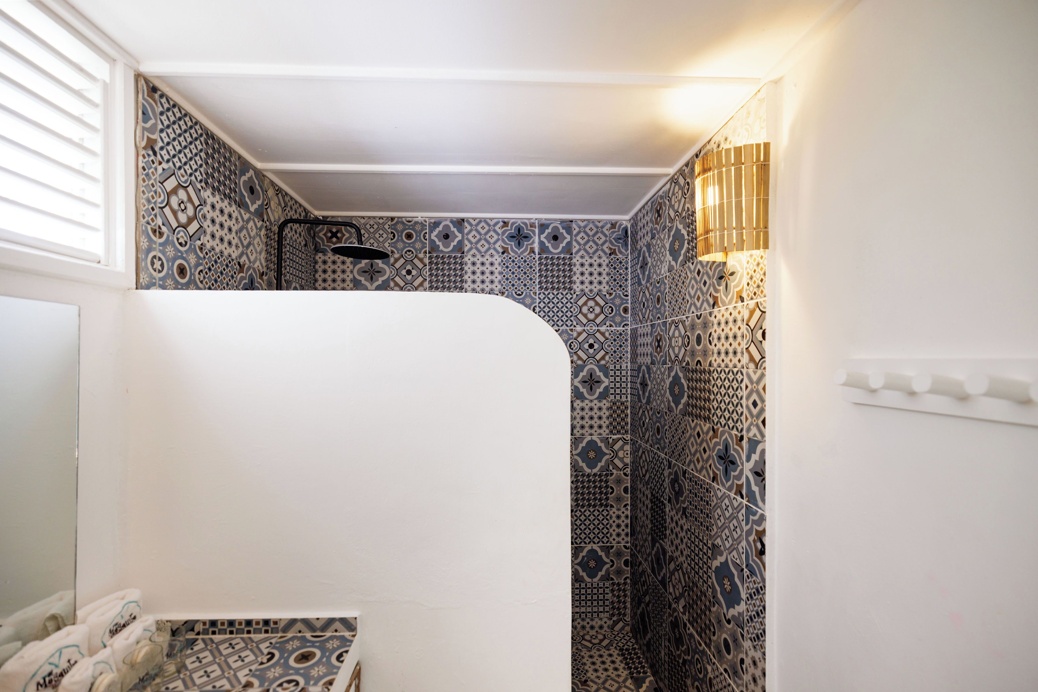 Un baño con baldosas estampadas, una bañera blanca y un aplique de pared.