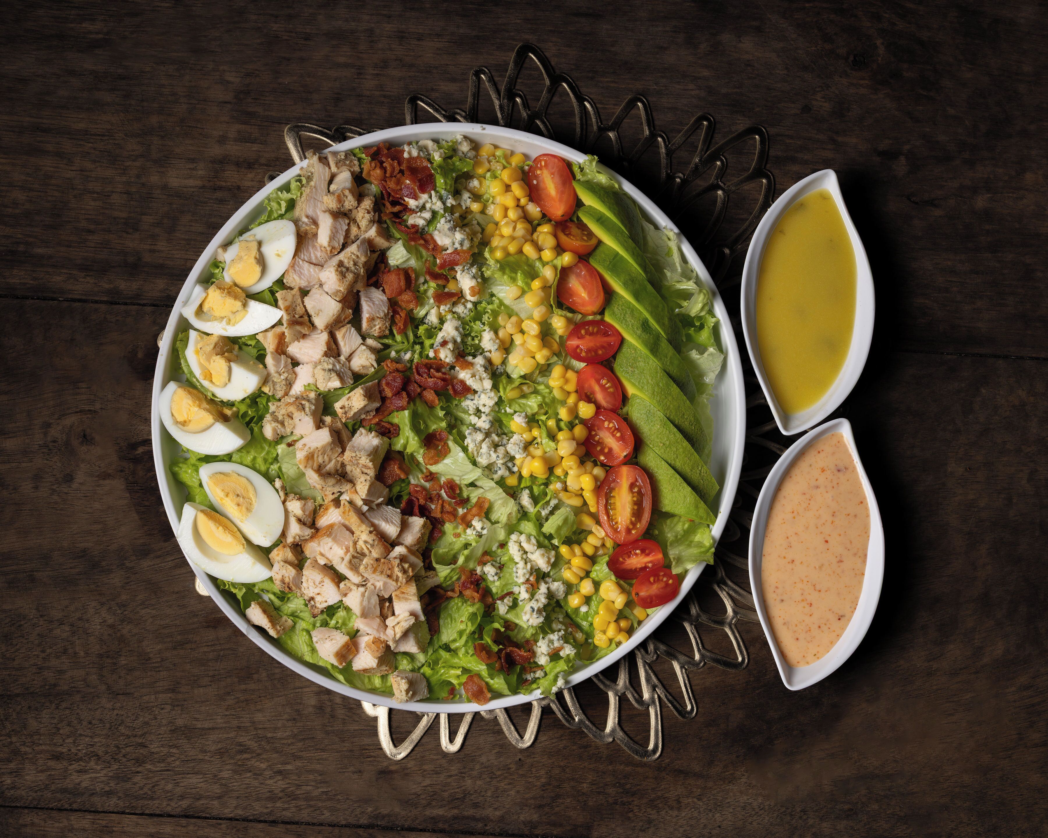 Un tazón de ensalada con diversos ingredientes y dos recipientes pequeños de aderezo.