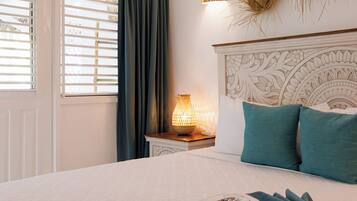 Quarto com cama, mesa de cabeceira, luminária e janela com cortinas.