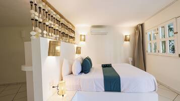 A hotel room with a bed, a wall-mounted light fixture, an air conditioning unit, and a window with curtains.