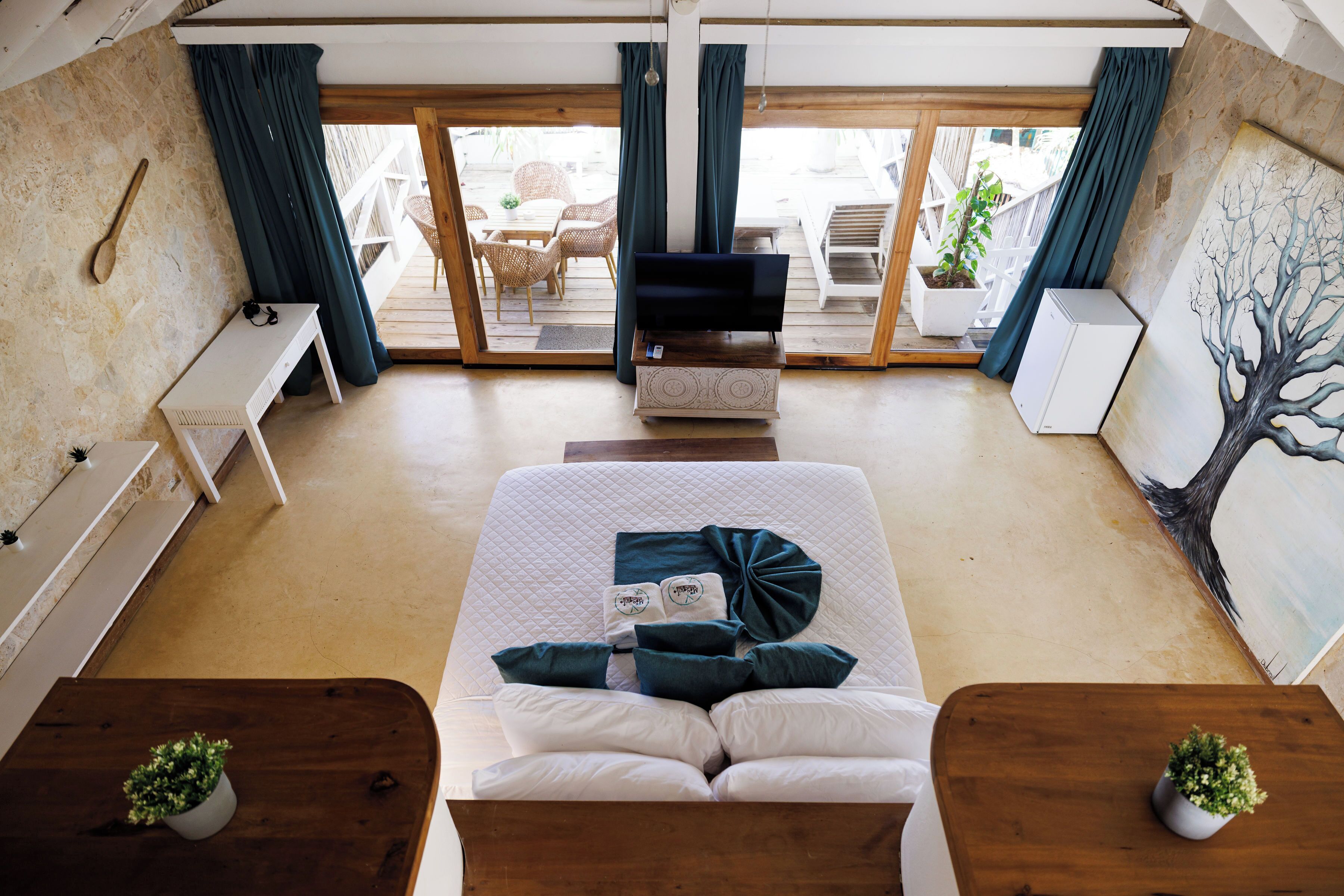 A bedroom with a bed, a TV, a desk, and a view of the outside.