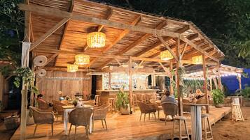 An outdoor wooden structure with a bar, wicker furniture, and hanging lights.