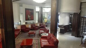 Um hall com sofás de couro vermelho, uma mesa de centro e um tapete estampado.