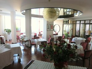 A restaurant interior with round tables, chairs, and a central decorative plant. - Hotel Internazionale (Cervignano del Friuli)