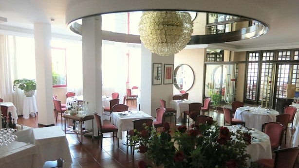 Interior de restaurante com mesas redondas, cadeiras e uma planta decorativa central.