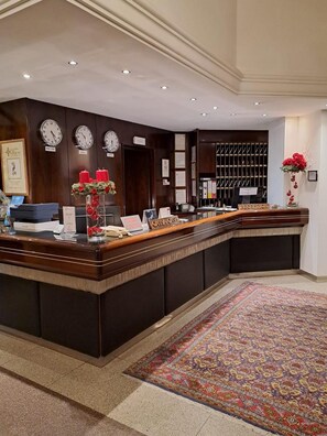 A reception desk with a clock, a red flower vase, and a reception sign. - Hotel Internazionale (Cervignano del Friuli)