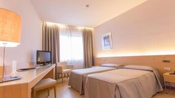 Ein Hotelzimmer mit zwei Betten, einem Schreibtisch mit Computer, einem Stuhl und einer Lampe.