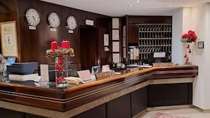 Uma mesa de recepção com um relógio, um vaso de flores vermelho e a placa da recepção.