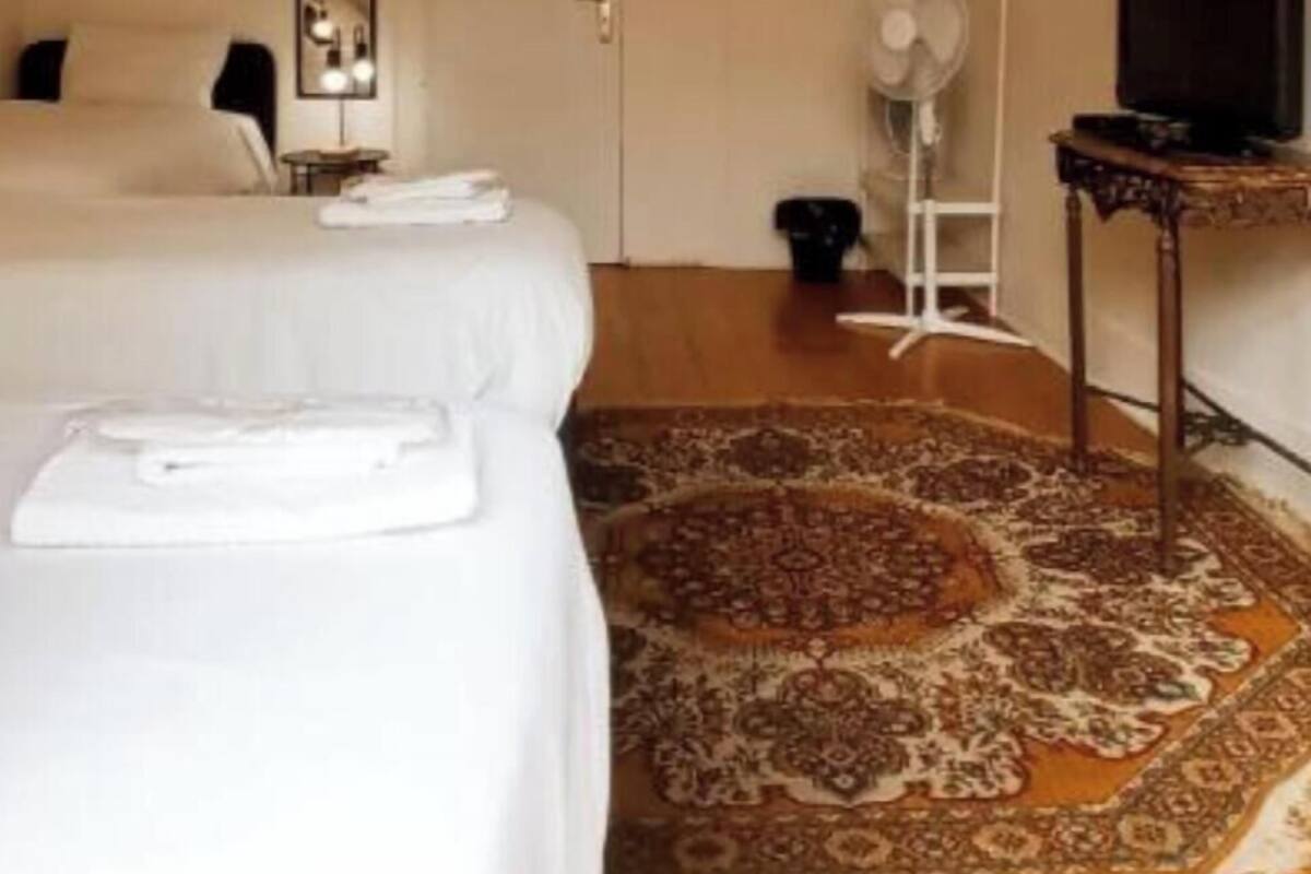A hotel room with two beds, a ceiling fan, a television, a mirror, and a patterned rug.