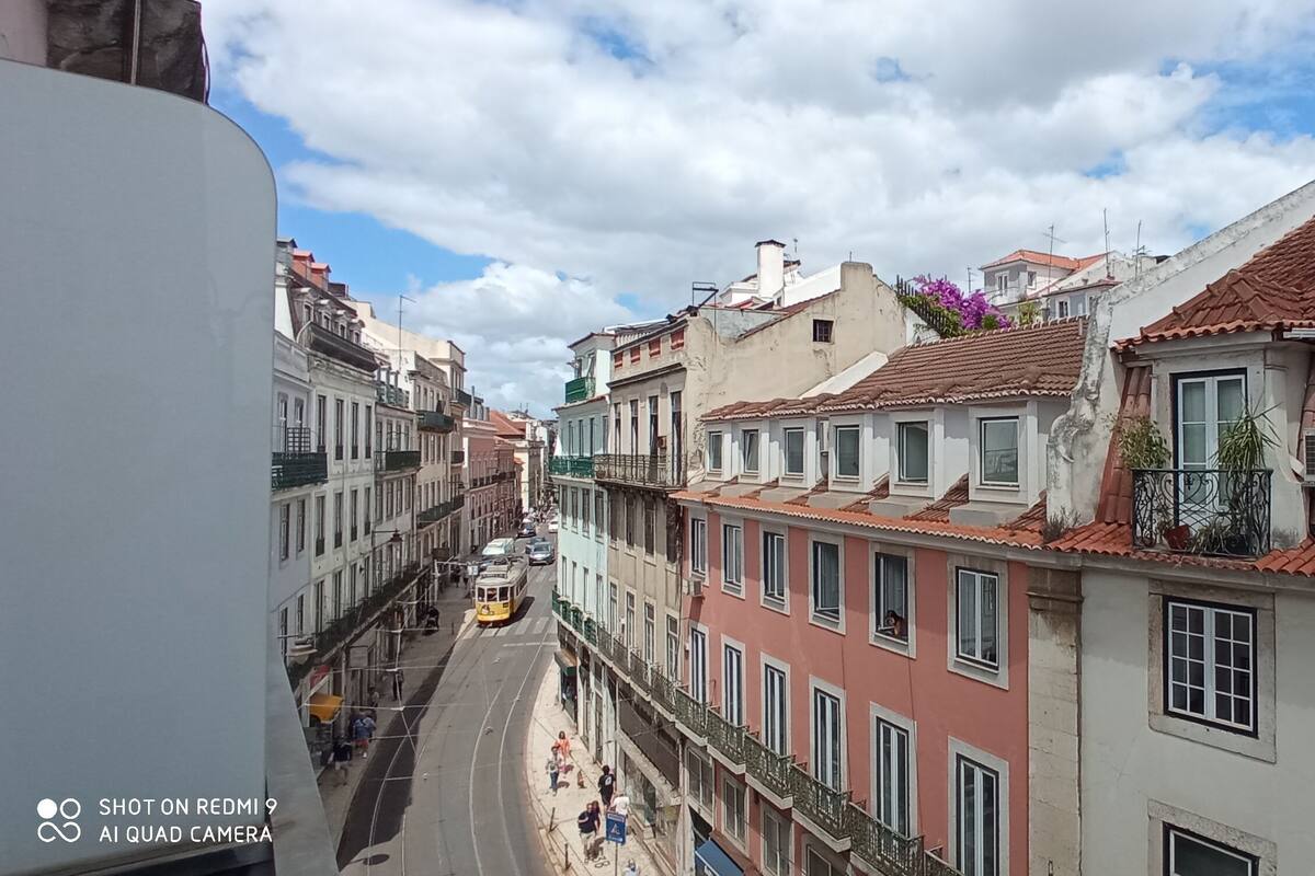A narrow street with multi-story buildings, balconies, and a tram.