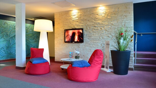 Un vestíbulo con pared de piedra, televisor de pantalla plana, sillones colgantes rojos, una mesa con lámpara y una planta grande en maceta.