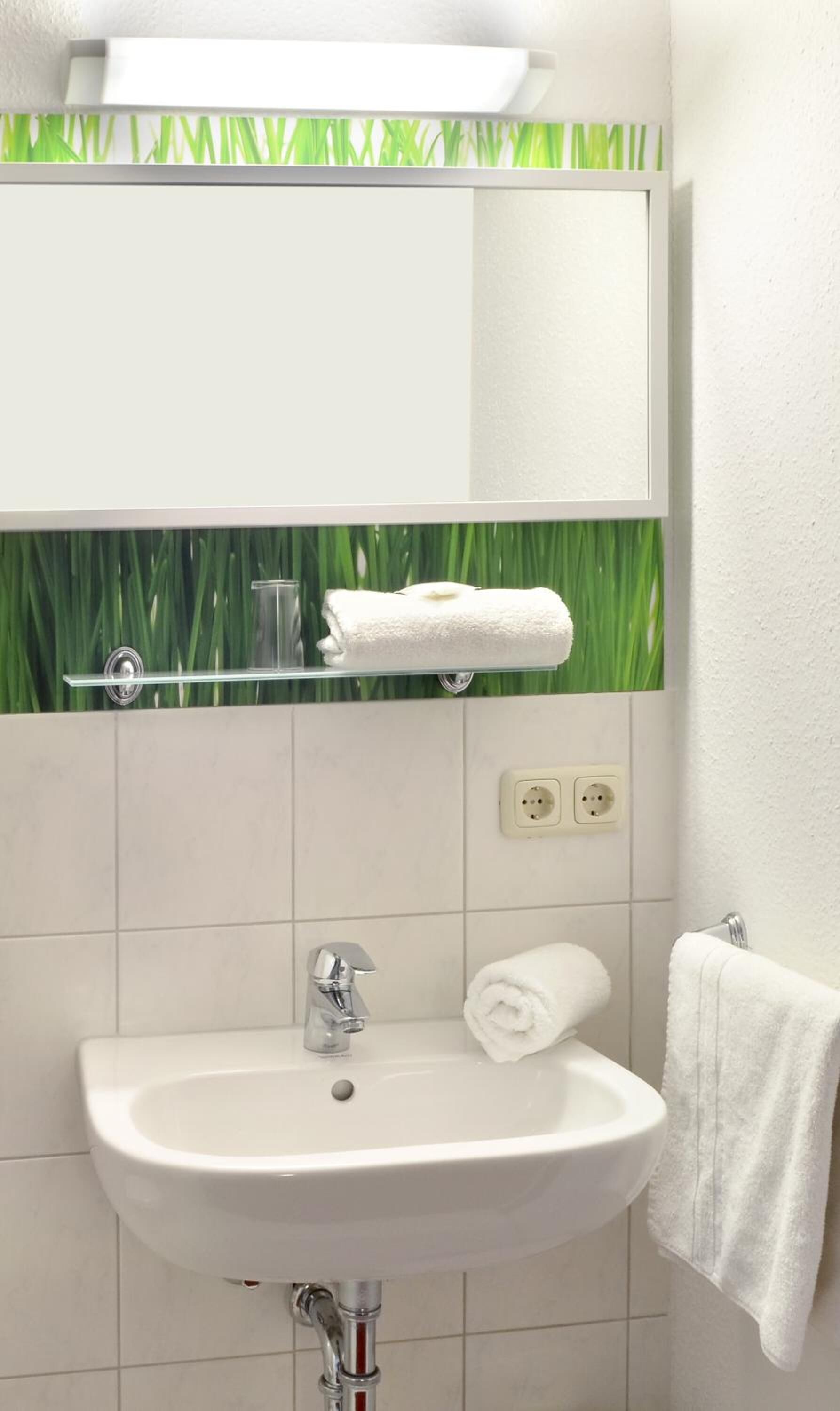 A bathroom with a white sink, a mirror, and a green grass-like backsplash.
