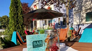 Una mesa de madera con un letrero que dice 'BAR', un tarro de cristal con bayas rojas y un paraguas en un entorno al aire libre.