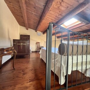 A room with a wooden ceiling, a bed with metal railings, a desk, and a chair.
